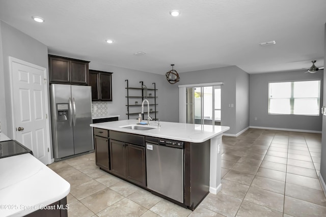 kitchen featuring appliances with stainless steel finishes, a sink, open floor plan, light countertops, and dark brown cabinetry