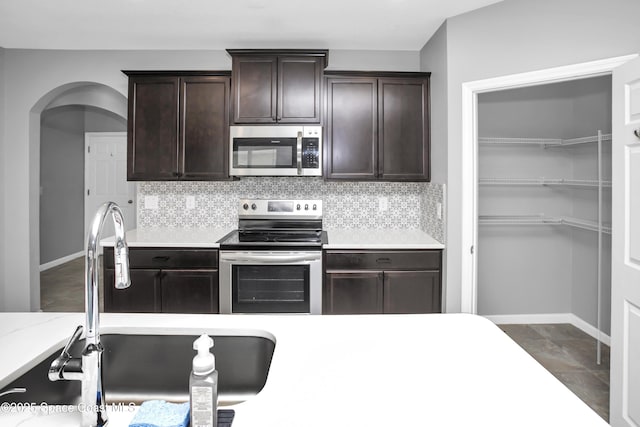 kitchen featuring stainless steel appliances, a sink, decorative backsplash, dark brown cabinets, and arched walkways
