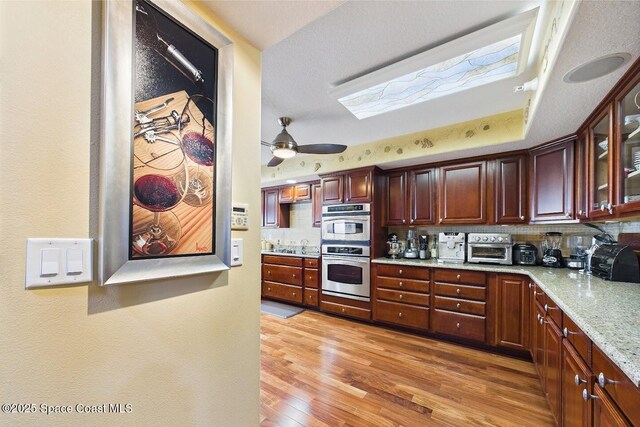 732 Bayside Dr Unit 501, Cape Canaveral, FL 32920 - kitchen featuring decorative backsplash, light wood-style flooring, double oven, glass insert cabinets, and light stone countertops