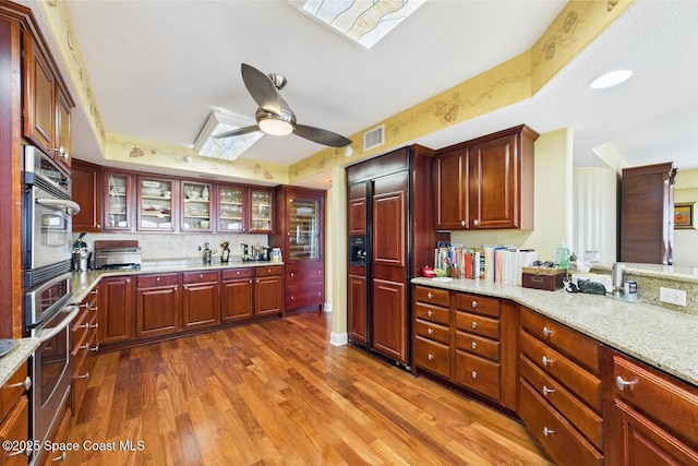 732 Bayside Dr Unit 501, Cape Canaveral, FL 32920 - kitchen with a skylight, a ceiling fan, dark wood-style flooring, glass insert cabinets, and light stone countertops