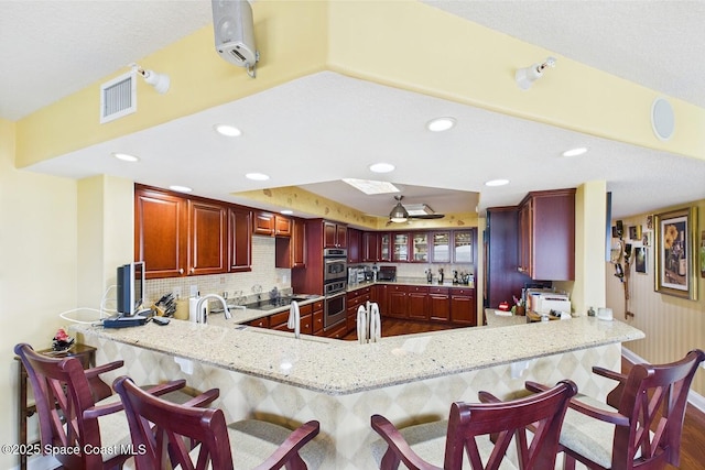 732 Bayside Dr Unit 501, Cape Canaveral, FL 32920 - kitchen with a peninsula, reddish brown cabinets, light stone countertops, tasteful backsplash, and recessed lighting