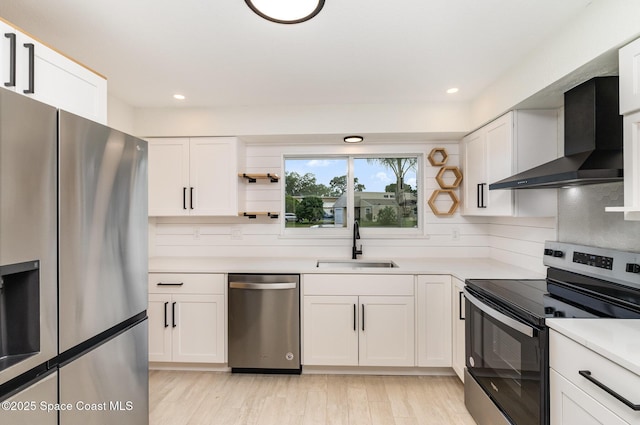 kitchen with stainless steel appliances, wall chimney range hood, a sink, white cabinetry, and light countertops