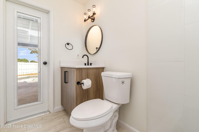 bathroom featuring toilet, baseboards, wood finished floors, and vanity