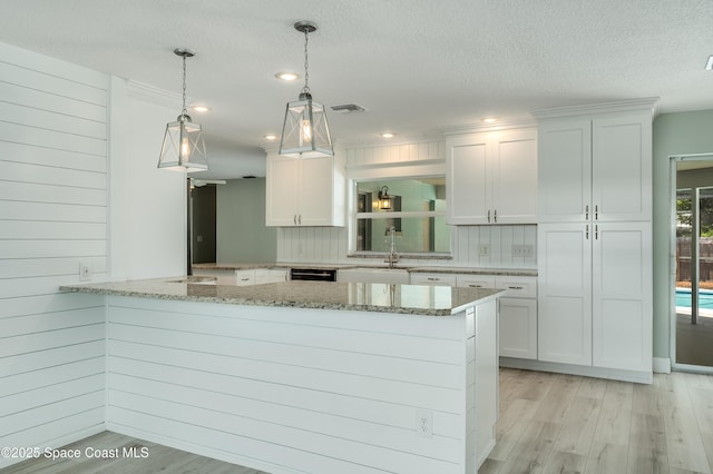 kitchen with white cabinets, light wood-type flooring, a peninsula, light stone countertops, and decorative light fixtures