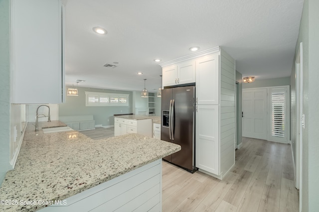 kitchen with stainless steel fridge with ice dispenser, a sink, white cabinetry, light stone countertops, and light wood finished floors