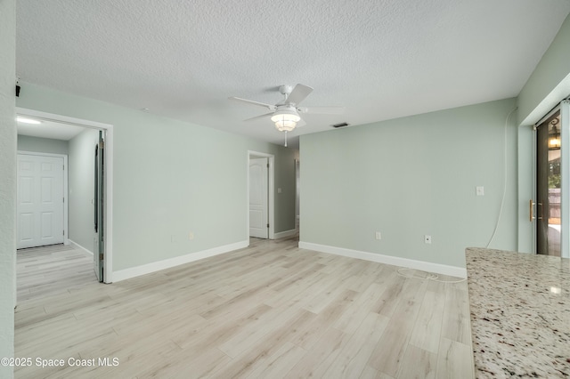 spare room featuring light wood-style floors, a ceiling fan, a textured ceiling, and baseboards