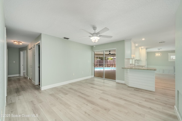 unfurnished living room with a ceiling fan, light wood-type flooring, a textured ceiling, and baseboards