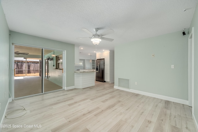 unfurnished living room with a ceiling fan, light wood-style flooring, baseboards, and a textured ceiling