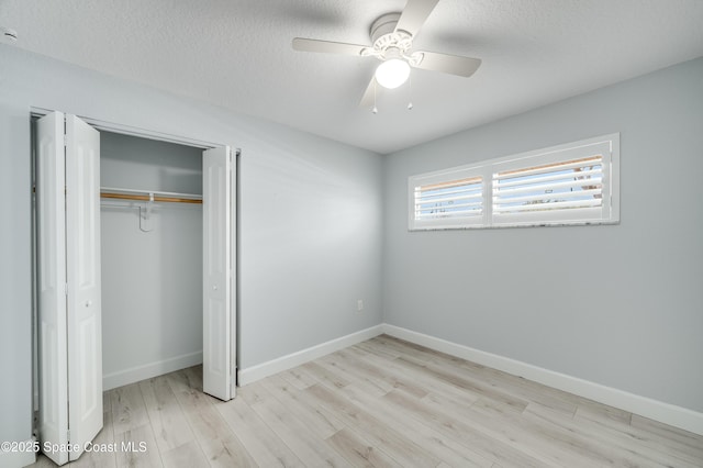 unfurnished bedroom featuring wood finished floors, a closet, a textured ceiling, baseboards, and ceiling fan