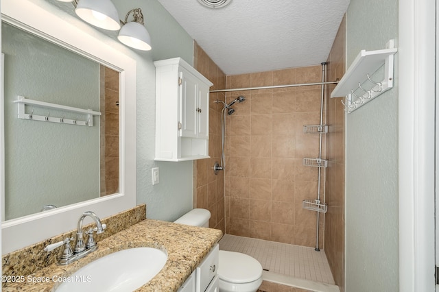 full bath featuring a tile shower, toilet, vanity, a textured wall, and a textured ceiling