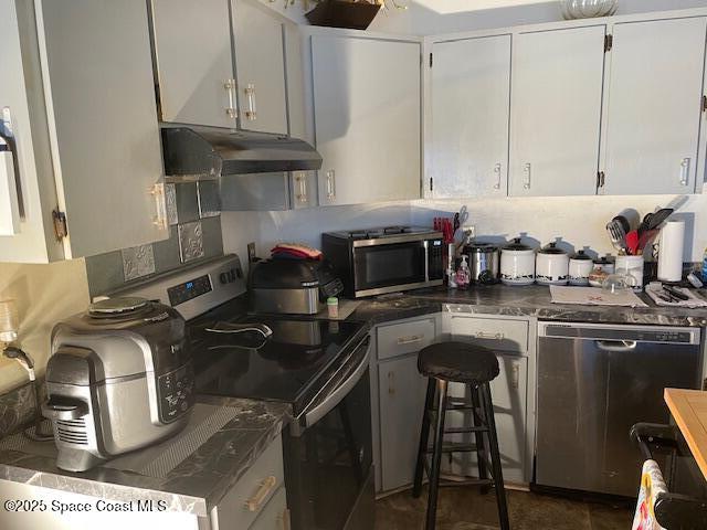 kitchen with under cabinet range hood, appliances with stainless steel finishes, dark countertops, and white cabinetry