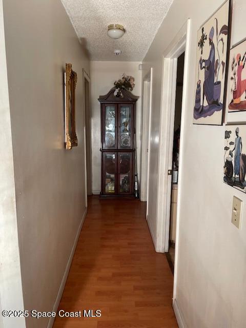 hall with a textured ceiling, wood finished floors, and baseboards