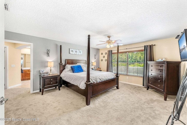 bedroom featuring light colored carpet, baseboards, arched walkways, ceiling fan, and a textured ceiling
