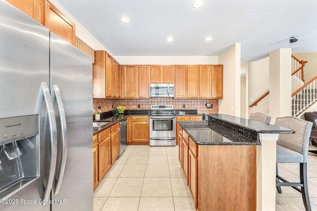 kitchen with appliances with stainless steel finishes, a breakfast bar, a kitchen island, backsplash, and light tile patterned flooring