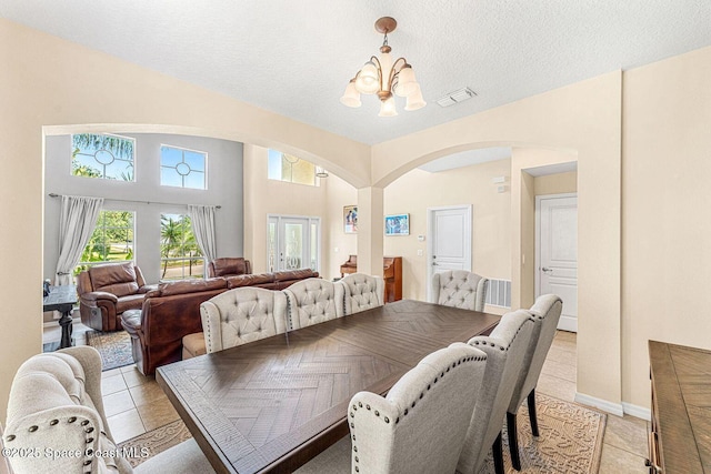 dining space featuring arched walkways, a chandelier, light tile patterned floors, a textured ceiling, and baseboards