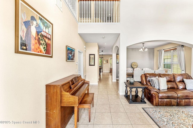 living room featuring arched walkways, light tile patterned flooring, a high ceiling, baseboards, and a chandelier