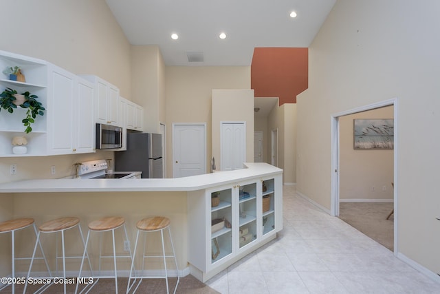 kitchen with appliances with stainless steel finishes, open shelves, a high ceiling, white cabinetry, and light countertops