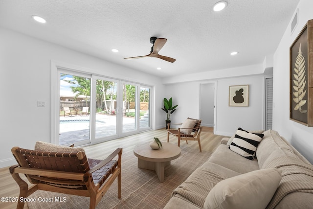living area with light wood-style flooring, recessed lighting, a ceiling fan, a textured ceiling, and baseboards
