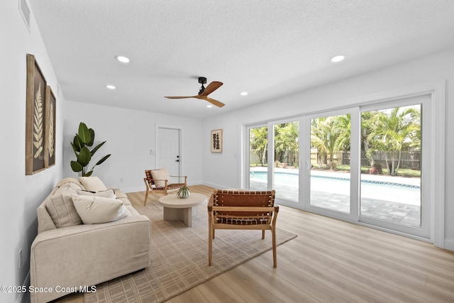 living room with light wood-type flooring, recessed lighting, a ceiling fan, baseboards, and a textured ceiling