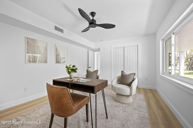 office area featuring light wood-type flooring, baseboards, a ceiling fan, and a textured ceiling