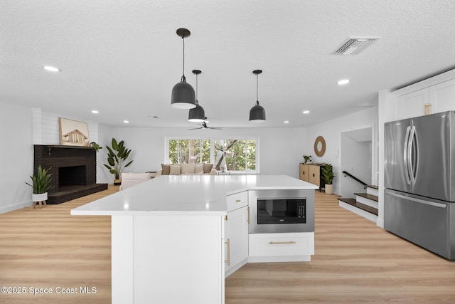 kitchen featuring freestanding refrigerator, built in microwave, light wood finished floors, open floor plan, and a fireplace