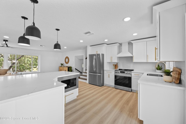 kitchen with appliances with stainless steel finishes, wall chimney exhaust hood, a sink, recessed lighting, and white cabinetry