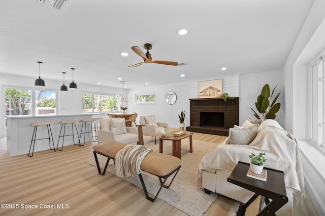 living room featuring light wood-style flooring, recessed lighting, a brick fireplace, and ceiling fan