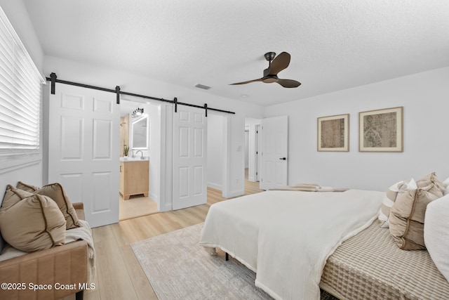bedroom with a barn door, light wood-type flooring, a textured ceiling, ensuite bathroom, and a sink