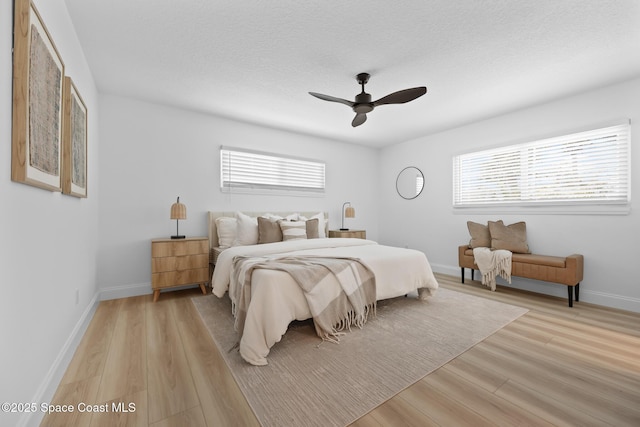 bedroom featuring multiple windows, light wood-type flooring, baseboards, a ceiling fan, and a textured ceiling