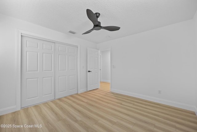 unfurnished bedroom with a closet, light wood finished floors, baseboards, a textured ceiling, and ceiling fan