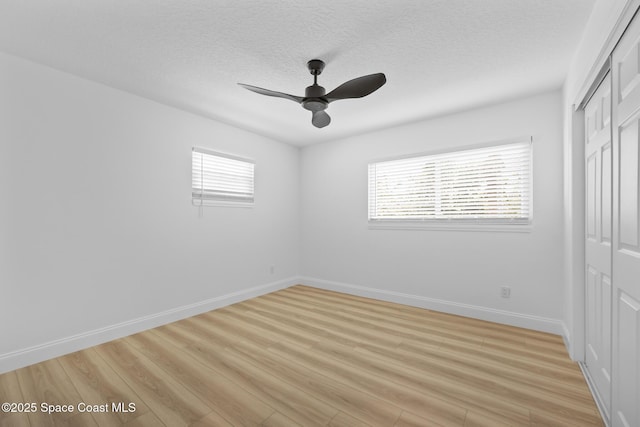 unfurnished bedroom with multiple windows, a closet, light wood-type flooring, and a textured ceiling