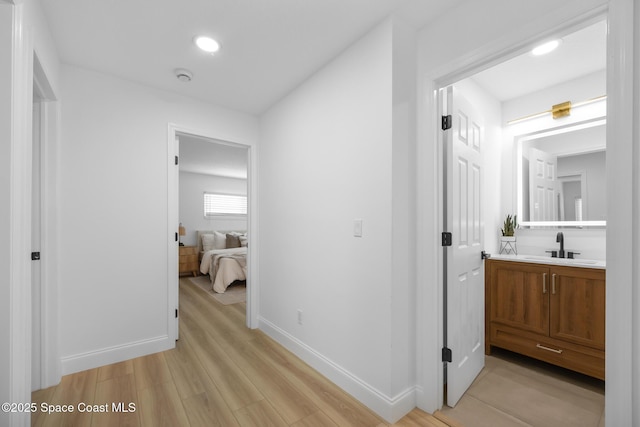 hall featuring light wood finished floors, a sink, baseboards, and recessed lighting