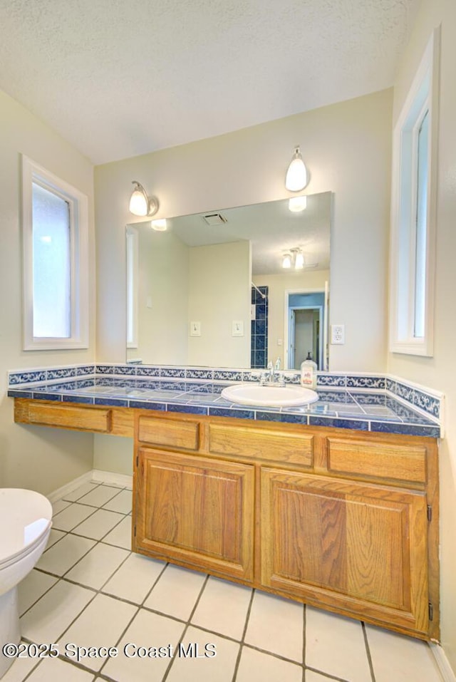 bathroom with tile patterned floors, toilet, vanity, baseboards, and a shower