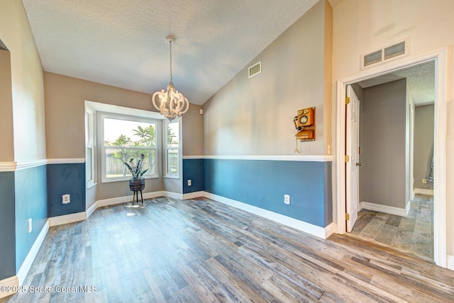 empty room featuring a chandelier, wood finished floors, vaulted ceiling, a textured ceiling, and baseboards