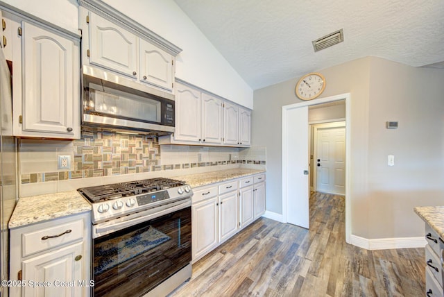 kitchen featuring stainless steel appliances, decorative backsplash, baseboards, light wood finished floors, and lofted ceiling
