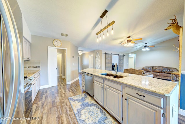 kitchen featuring appliances with stainless steel finishes, a sink, a ceiling fan, a barn door, and light wood finished floors