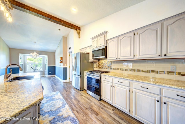 kitchen featuring stainless steel appliances, a sink, light wood-style flooring, decorative backsplash, and light stone counters