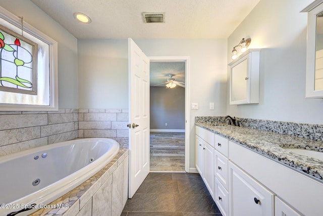 bathroom with ceiling fan, a textured ceiling, a jetted tub, double vanity, and baseboards