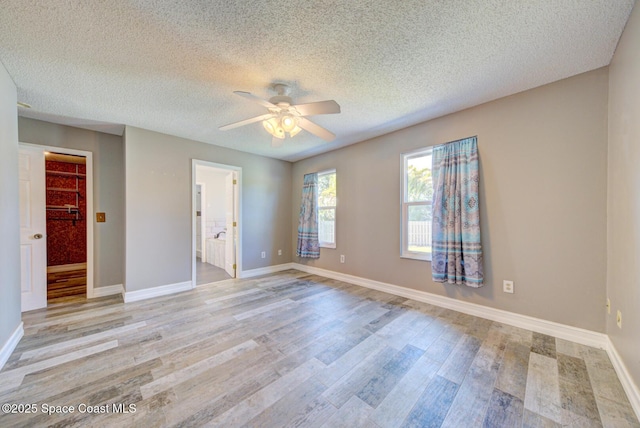 unfurnished bedroom with light wood-type flooring, baseboards, a spacious closet, a textured ceiling, and a ceiling fan