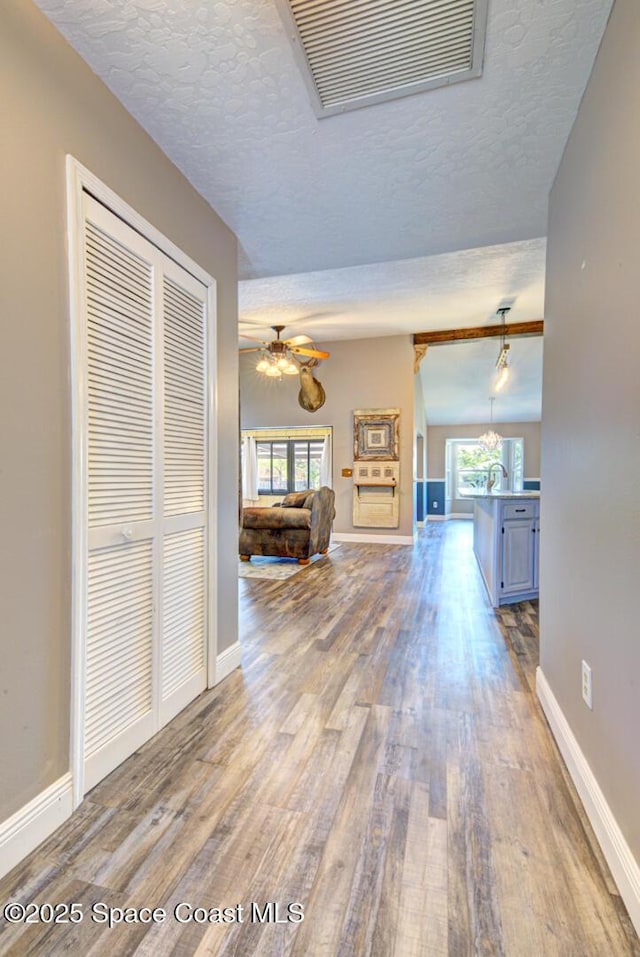 hall featuring wood finished floors, baseboards, and a textured ceiling