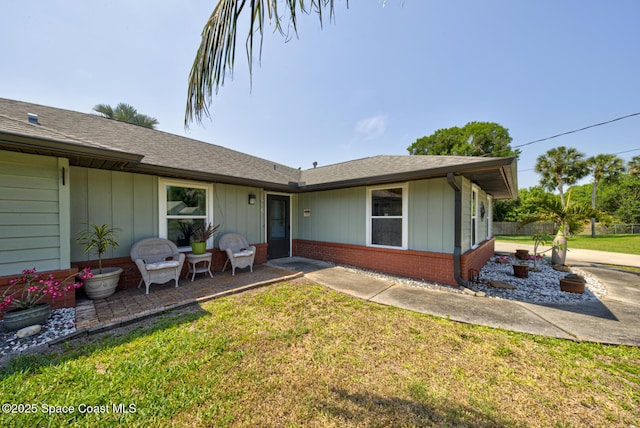 rear view of property with a lawn, a patio, board and batten siding, and brick siding