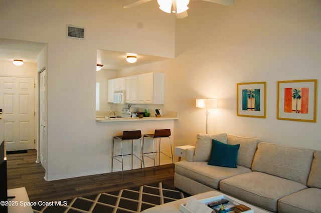 living area featuring dark wood-type flooring, ceiling fan, and a towering ceiling