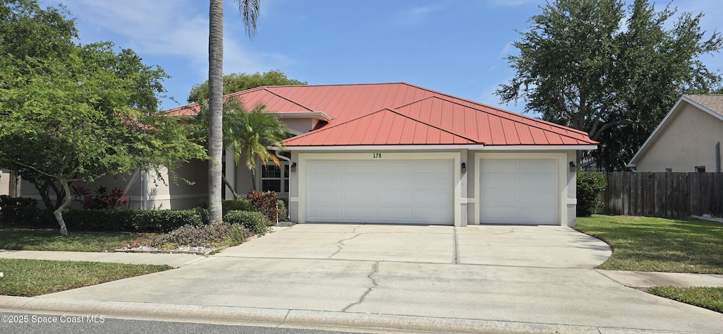 view of front of property featuring driveway, stucco siding, fence, a standing seam roof, and a garage
