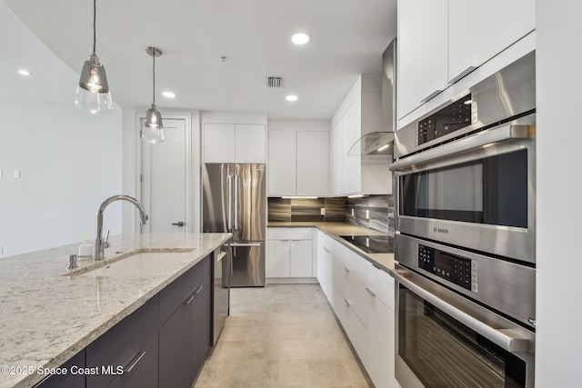 kitchen with a sink, modern cabinets, appliances with stainless steel finishes, white cabinetry, and hanging light fixtures
