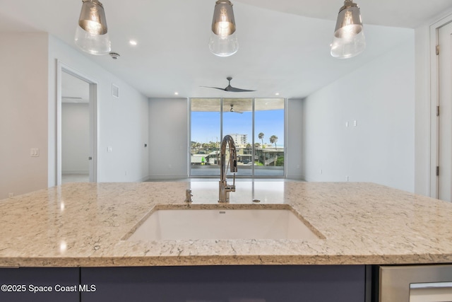 kitchen featuring a sink, open floor plan, a ceiling fan, light stone counters, and hanging light fixtures