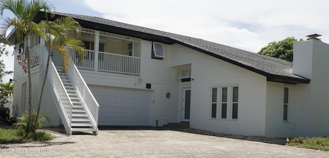 back of property with stairs, an attached garage, decorative driveway, stucco siding, and a shingled roof