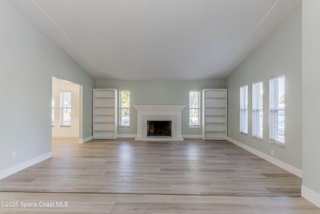 unfurnished living room with a fireplace, vaulted ceiling, baseboards, and wood finished floors