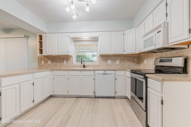 kitchen featuring white appliances, a sink, white cabinetry, and light wood-style flooring