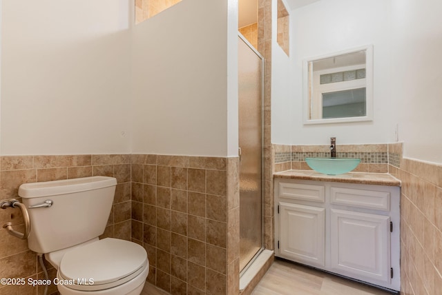 full bathroom with tile walls, a wainscoted wall, a shower stall, toilet, and vanity