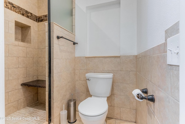 bathroom featuring tile walls, a shower stall, toilet, and a wainscoted wall
